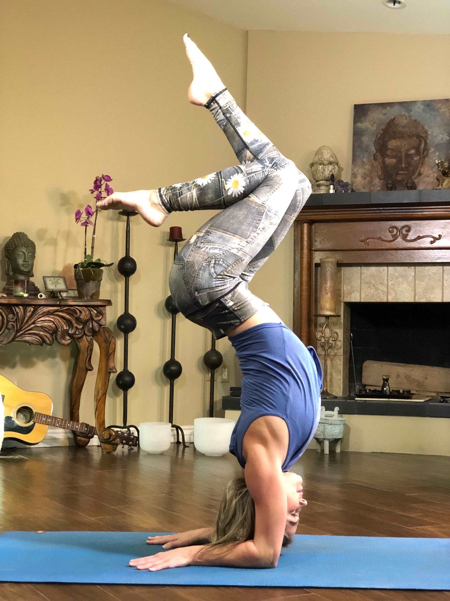 Woman wearing black tie-front tank top with geometric flower on it and leggings doing headstand.